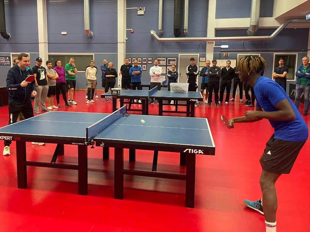 Bordtenniskamp med tilskuere rundt bordet