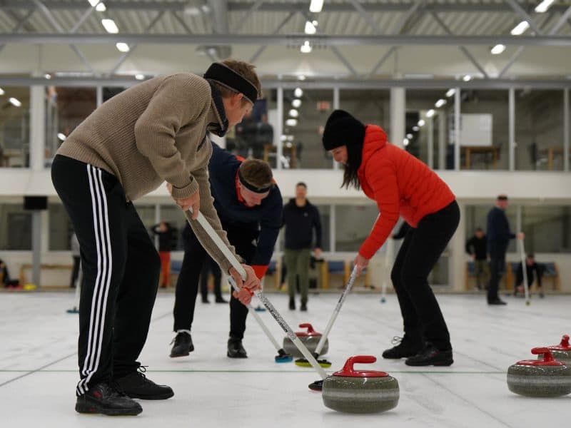 Tre medlemmer koster foran curlingsteinen