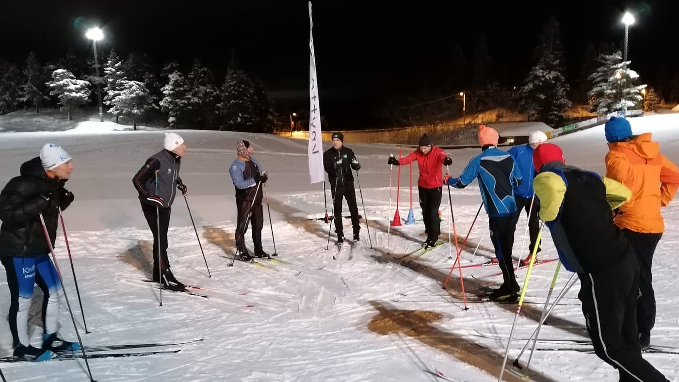 Medlemmer på langrennsski får teknikktips av instruktør i lysløypa