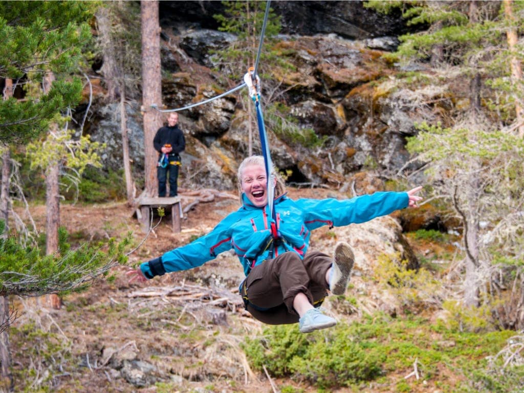 Jublende deltaker i blå jakke suser gjennom skogen på zipline